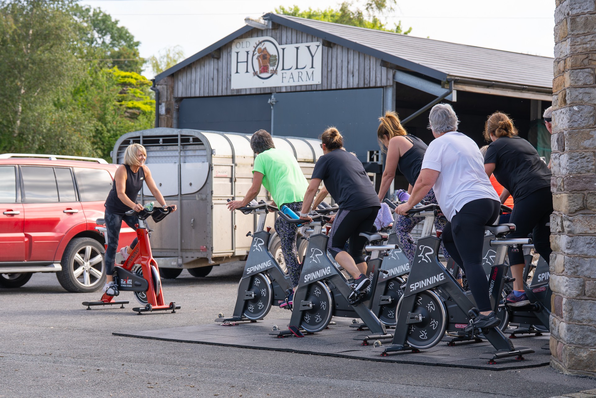 A spin class in the farmyard outside the Old Holly Farm barn, coach on a red bike at the front
