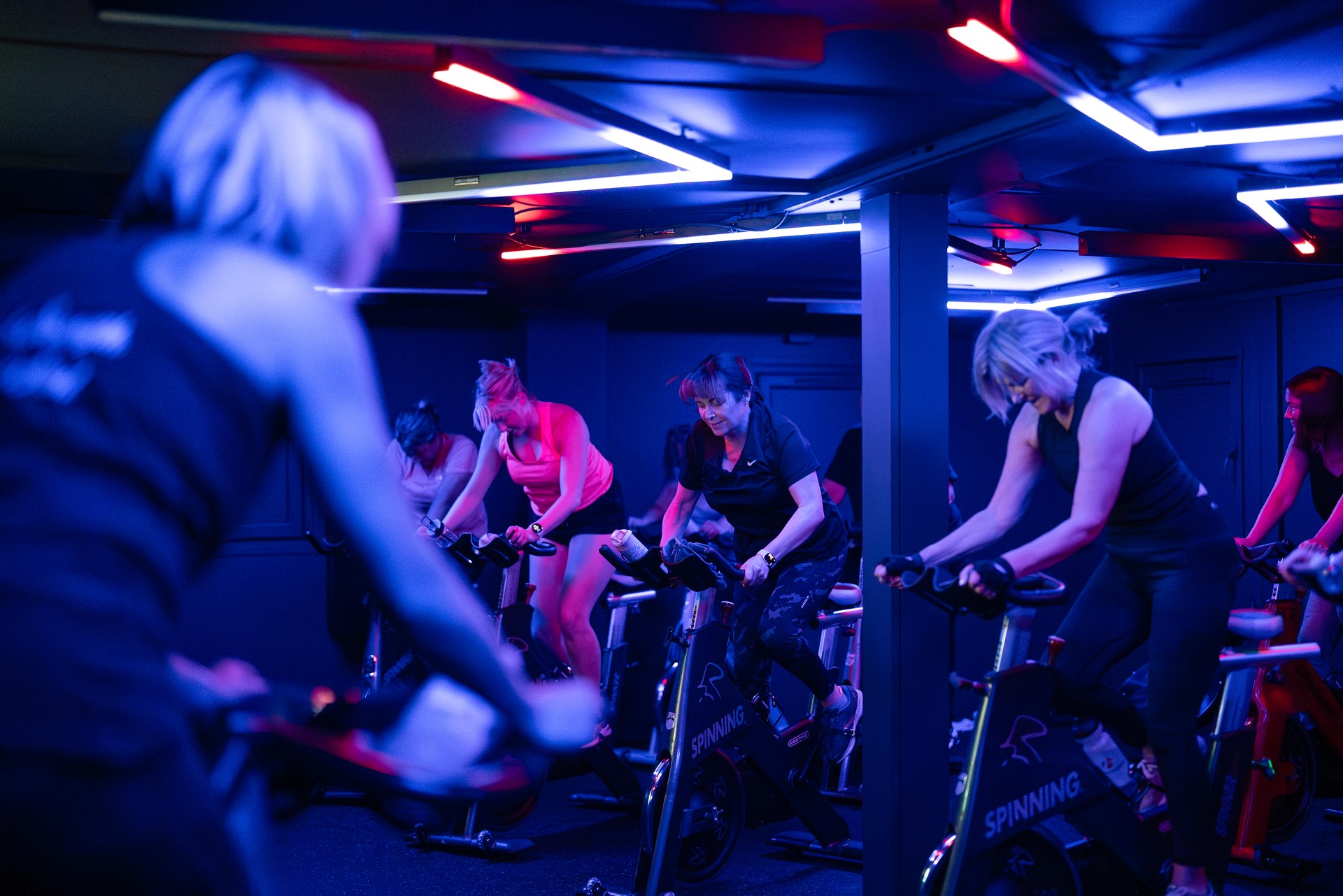 A full spin class riding under the neon ceiling of The Vault
